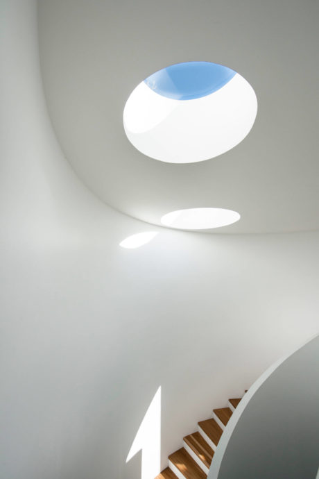 White minimalist stairway with circular skylights casting light on the walls.
