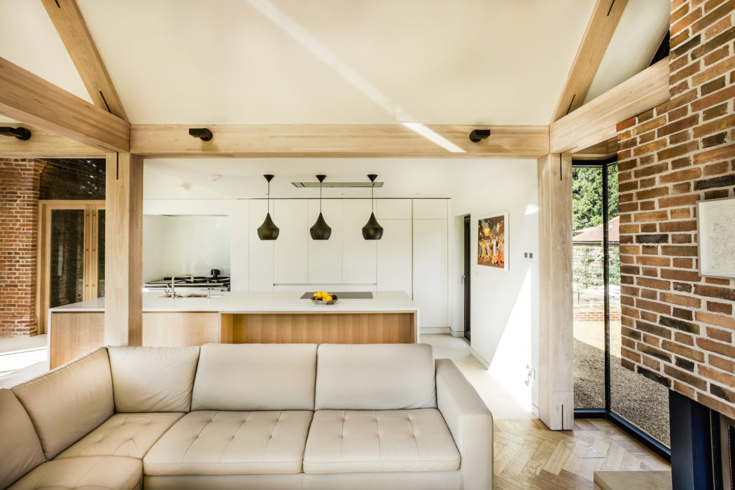 Modern living room with exposed beams, white sofa, and kitchen in the background.