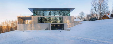 Modern glass house on a snowy hillside with clear skies.