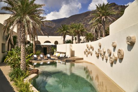 Luxurious poolside with loungers, palm trees, and decor against a mountain