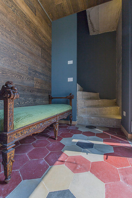 An antique bench against a wooden wall in a room with colorful hexagonal floor tiles