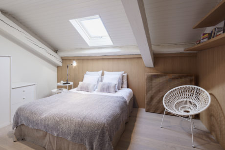 Contemporary attic bedroom with skylight, wooden walls, and designer chair.