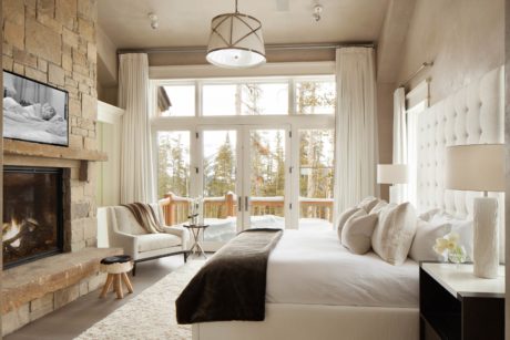 Modern bedroom with a fireplace, large windows, and neutral tones.