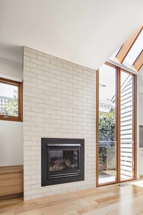 Modern room with white brick fireplace, wooden floors, and large windows.