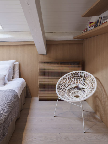 Cozy wooden bedroom interior with modern white chair and bed.