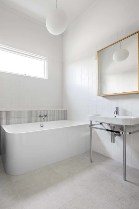 Minimalist white bathroom with bathtub, sink, and pendant lights.