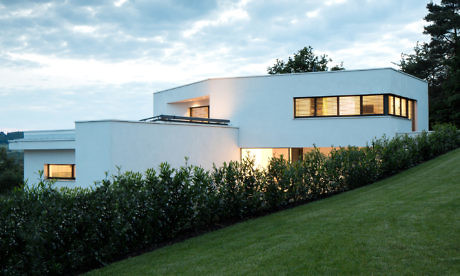Modern white house with illuminated windows at dusk.