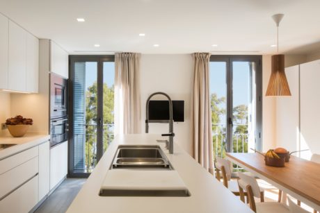 Modern kitchen interior with white countertops and a dining table, overlooking a balcony.