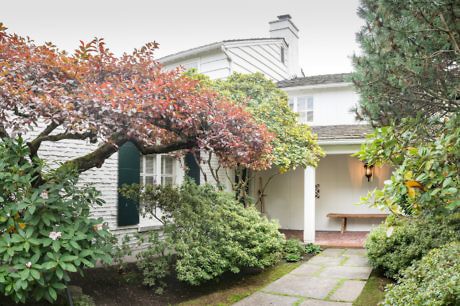 Charming house front with lush garden and draped tree.
