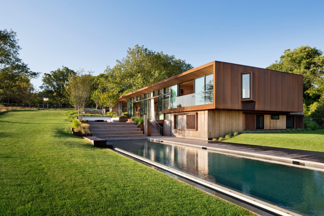 Modern house with large glass windows, wooden exterior, and a long narrow pool.