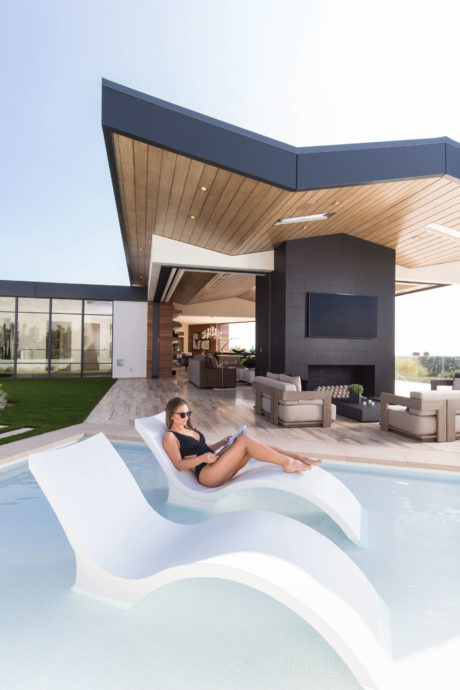 Woman relaxing on a pool lounger with a modern house in the background.