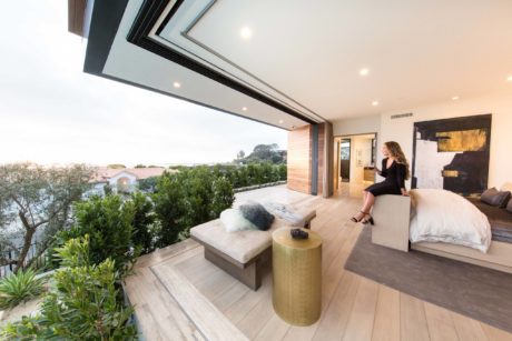 Modern bedroom with open terrace overlooking a scenic view, with a person seated.