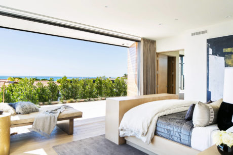 Modern bedroom with open sliding door to seaside view.