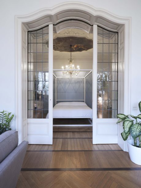 Elegant arched doorway with reflective doors leading to a bedroom with a classic ch