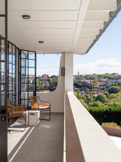 Balcony with chairs overlooking a green landscape, framed by glass doors.