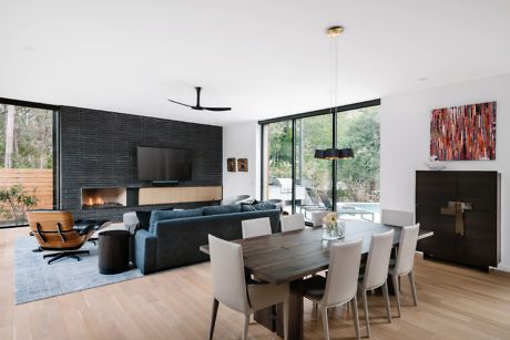 Modern living room with a fireplace, sofa, dining area, and large windows.