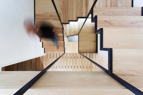 Contemporary wooden staircase with black accents and blurred person descending.