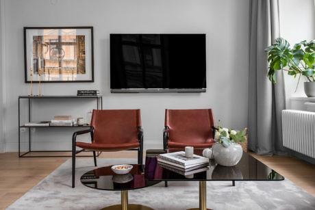 Modern living room with two leather chairs, a TV on wall, and a glass