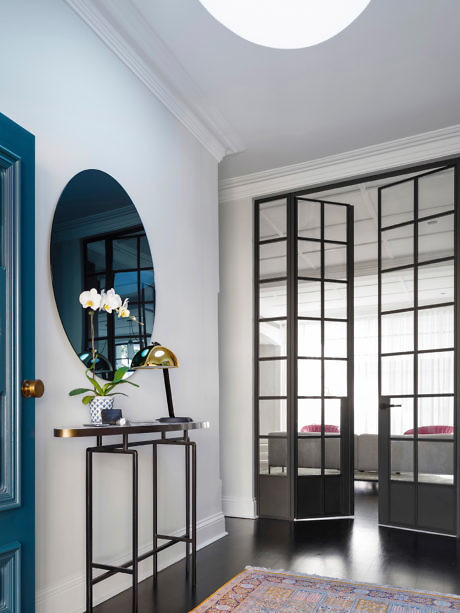Chic interior with blue door, oval mirror, and black-framed glass doors