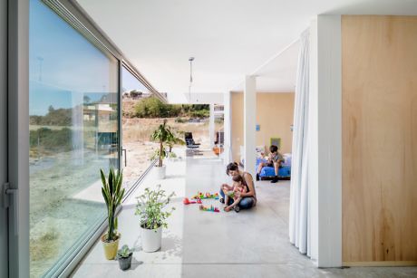 Bright, open-plan living space with floor-to-ceiling windows and a person playing