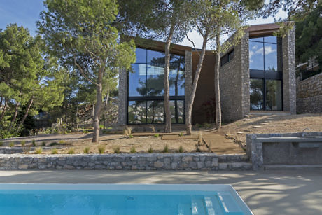 Contemporary glass house with stone accents by a pool.