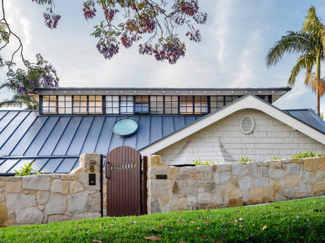 Suburban house with a stone fence, wooden gate, and a blue roof.