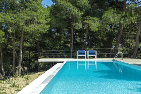 Outdoor swimming pool with a lounge chair surrounded by trees.