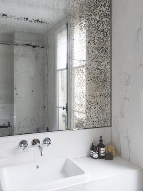 Modern bathroom with marble walls, a white sink, and a moldy mirror.