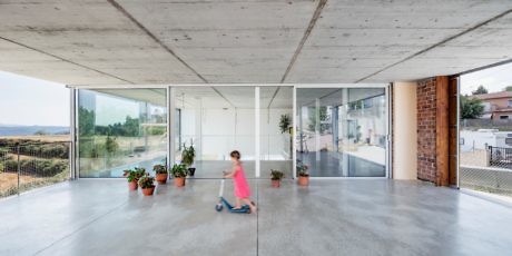 Modern open space with large glass doors, a child playing, and exposed concrete ceiling