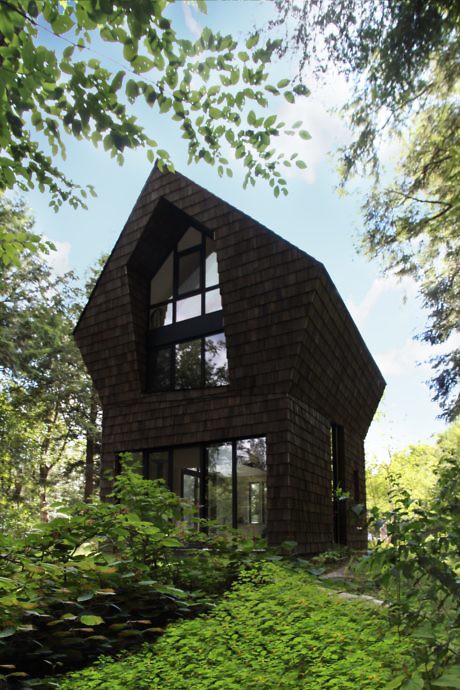 Modern A-frame house with large windows nestled in a lush forest setting.