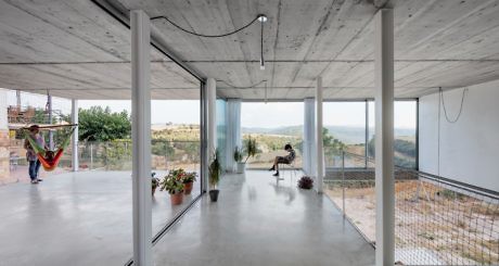 Minimalist room with large windows, concrete pillars, and two people relaxing.