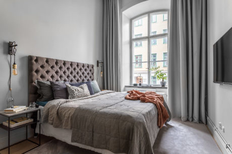 Modern bedroom with a tufted headboard, neutral bedding, and large windows