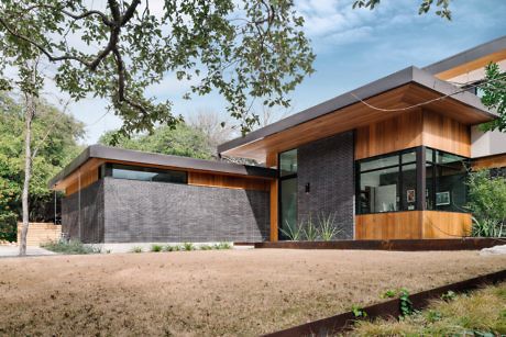 Modern house with large glass windows and wood paneling surrounded by trees.