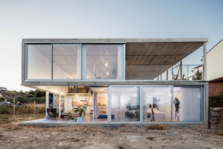 Modern two-story glass house with concrete accents at dusk.