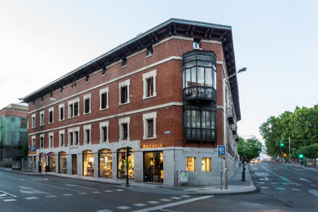 Corner view of a traditional red brick building with a glass balcony at dusk.