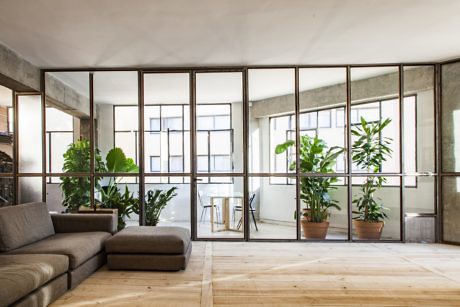 Industrial-style room with large windows and green plants.
