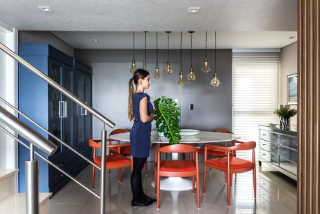 Woman standing in a modern kitchen with blue cabinets and red chairs.
