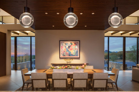 Modern dining room with large table, pendant lights, and sunset view.