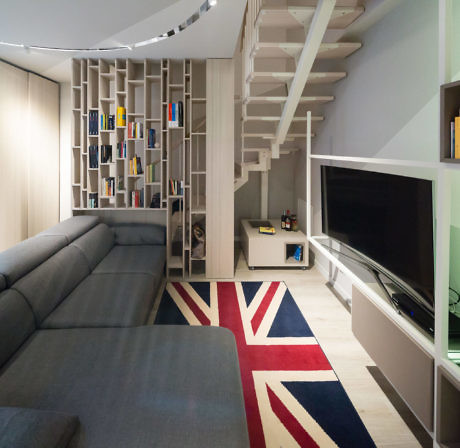 Modern living room with a bookshelf, staircase, and British flag rug.