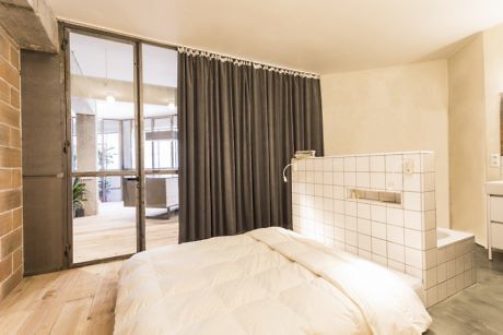 Contemporary bedroom with exposed brick, open bathroom concept, and glass partition.