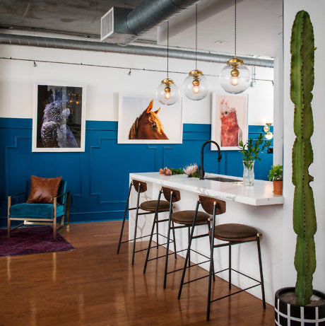 Modern kitchenette with bar stools, blue walls, and art decor.