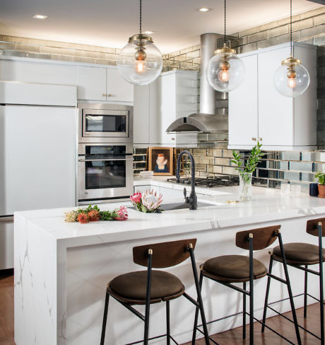 Modern kitchen with white island, bar stools, and pendant lighting.