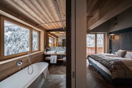 Cozy wooden cabin interior with bedroom and bathroom overlooking snowy landscape.