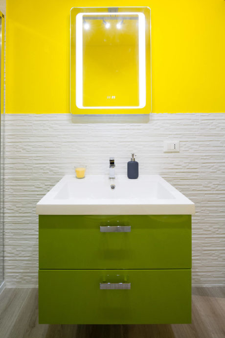 Vibrant yellow bathroom wall with a green vanity cabinet and a white basin.