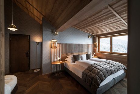 Cozy wooden bedroom interior with a large bed and snowy view outside.