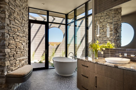 Contemporary bathroom with stone walls, freestanding tub, and large windows.