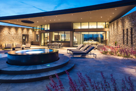 Modern house with large windows, courtyard, and fire pit at dusk.