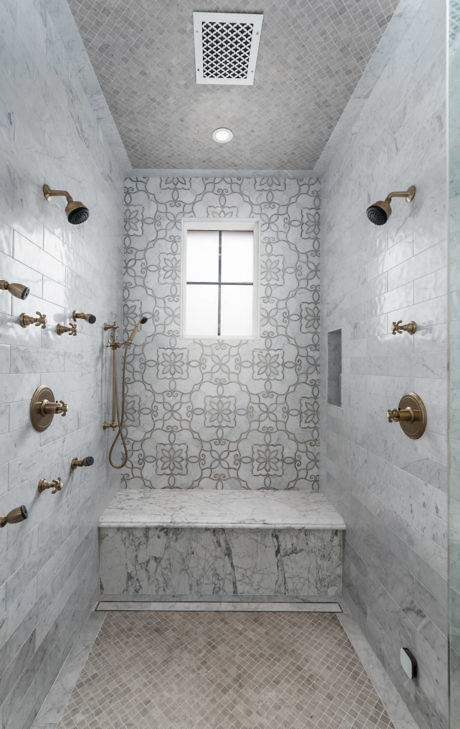 Modern marble tiled bathroom with multiple showerheads and patterned accent wall.