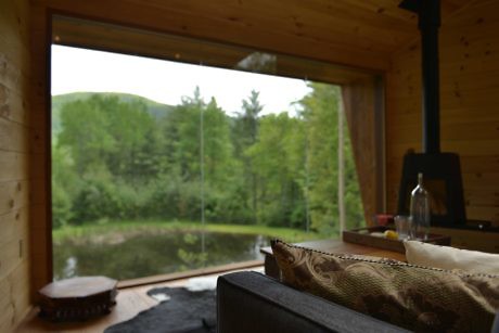 Wooden cabin interior with large window overlooking a serene lake.