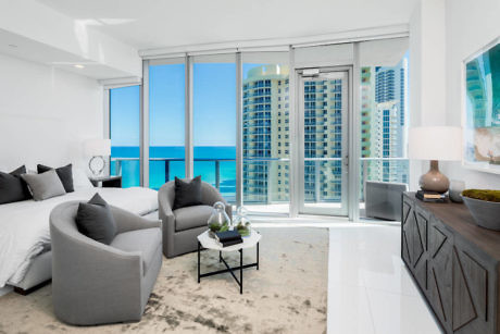 Modern bedroom with ocean view through floor-to-ceiling windows.